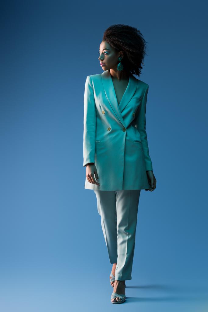  atractiva mujer afroamericana en traje mirando hacia otro lado sobre fondo azul
  - Foto, imagen