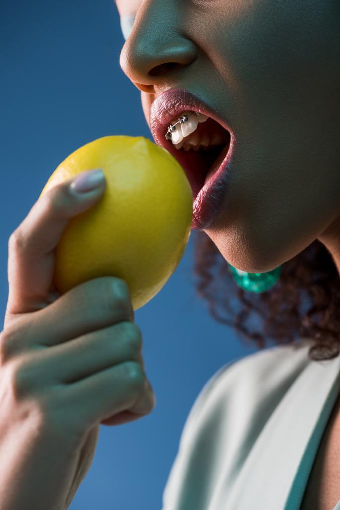 vue recadrée de femme afro-américaine avec bretelles mangeant du citron isolé sur bleu
 - Photo, image