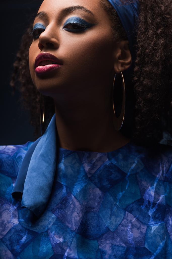 κομψή Αφροαμερικανή γυναίκα με σκουλαρίκια κοιτάζοντας κάμερα απομονωμένη σε μαύρο - Φωτογραφία, εικόνα