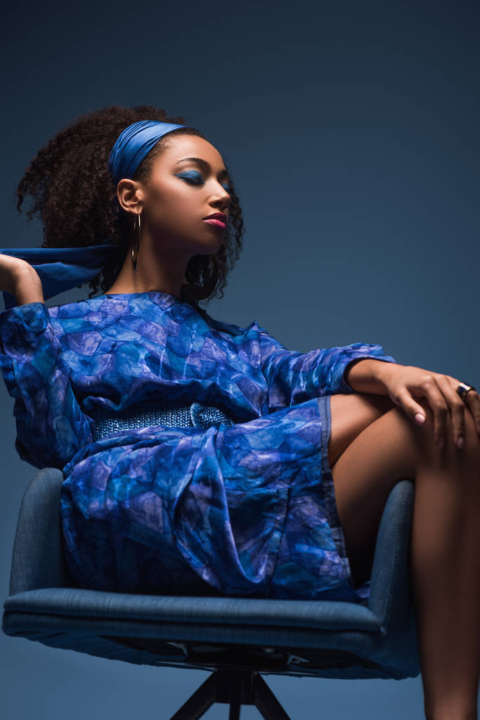 vonzó afro-amerikai nő csukott szemmel ül karosszéken elszigetelt kék - Fotó, kép
