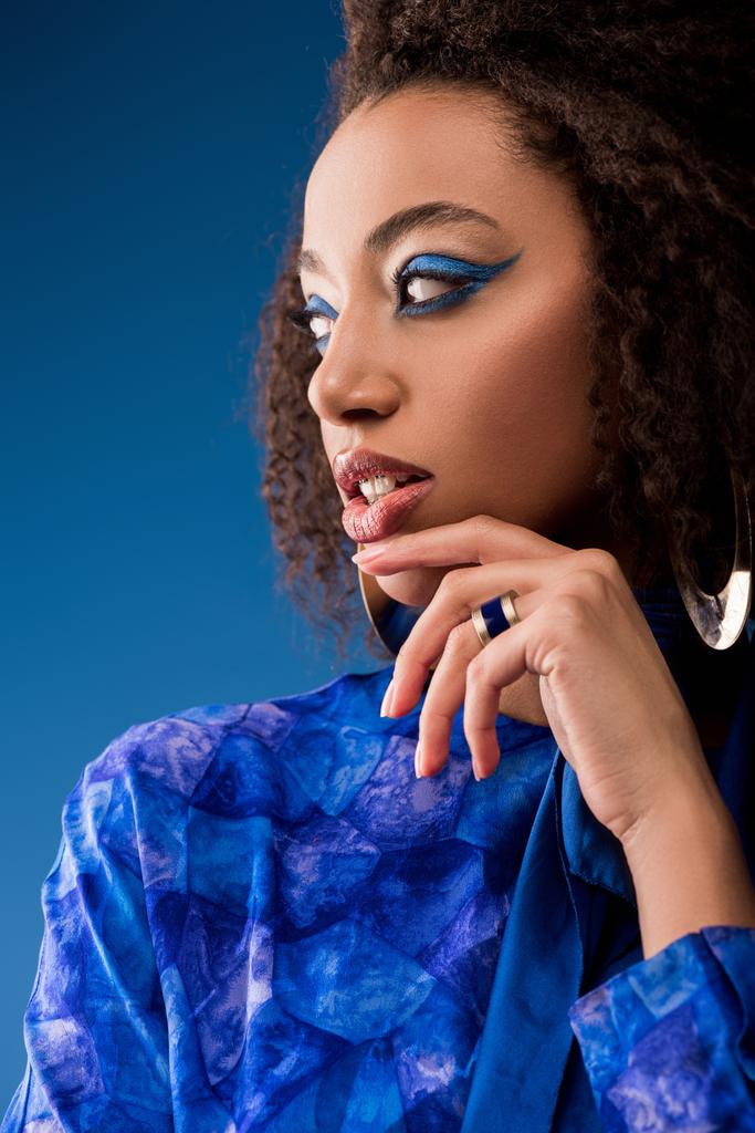 attraente donna afro-americana con il trucco in abito guardando lontano isolato sul blu
  - Foto, immagini