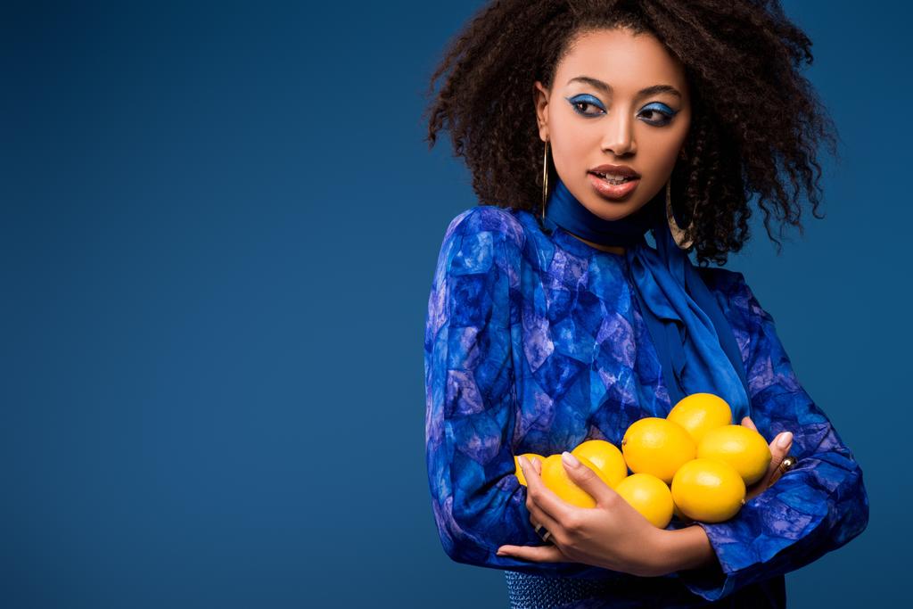séduisante femme afro-américaine tenant citrons isolés sur bleu
  - Photo, image