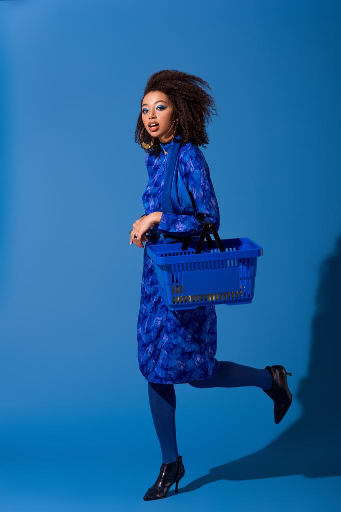 Африканская американка держит корзину для покупок на синем фоне
  - Фото, изображение
