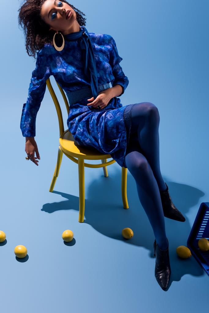 afro-amerikai nő ül széken csukott szemmel kék háttér  - Fotó, kép