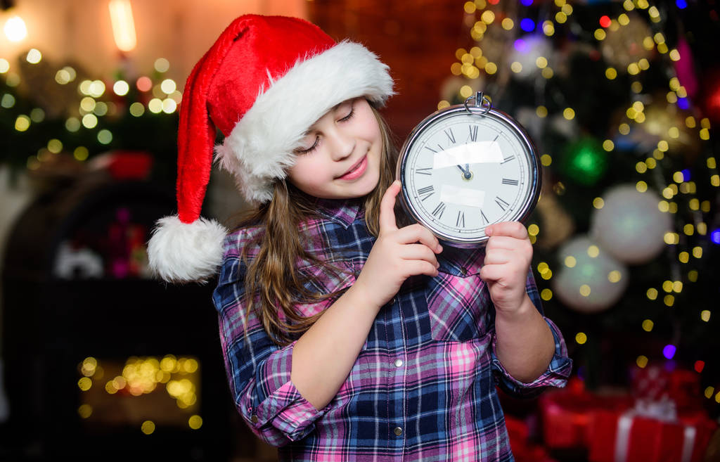 Пришло Рождество. Время праздновать. С Новым годом. Эльфийское дитя с часами. Рождественское дерево. С праздником. Маленькая девочка в красной шляпе. Счастливого Рождества. Маленькая девочка Санта Клауса. Время Рождества - Фото, изображение