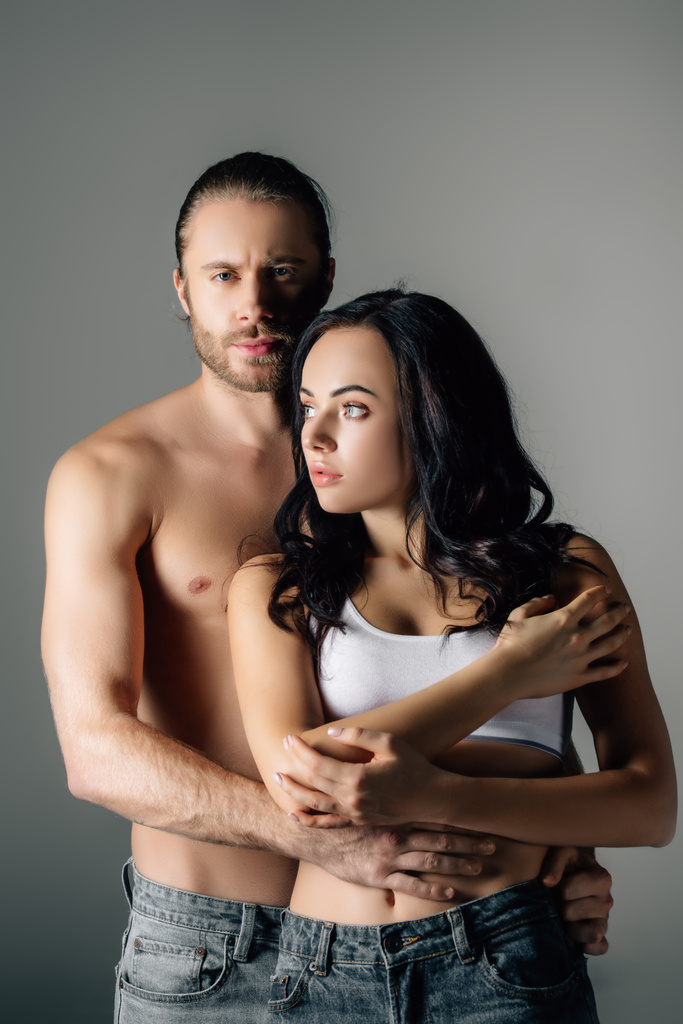 γυμνόστηθος νεαρός άνδρας αγκαλιάζει ελκυστική γυναίκα απομονωμένη στο γκρι   - Φωτογραφία, εικόνα