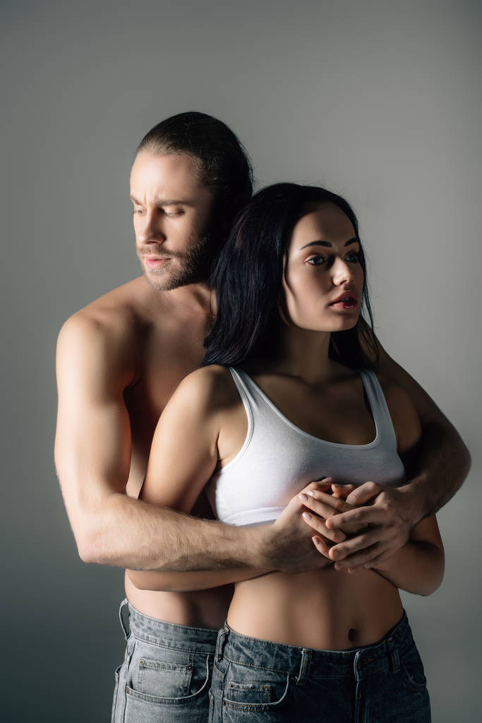 verführerischer Mann umarmt attraktive Freundin isoliert auf grau   - Foto, Bild