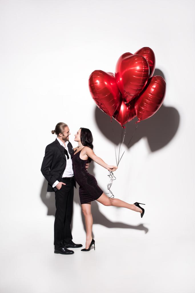 Lächelndes Paar mit roten herzförmigen Luftballons am Valentinstag auf weiß - Foto, Bild