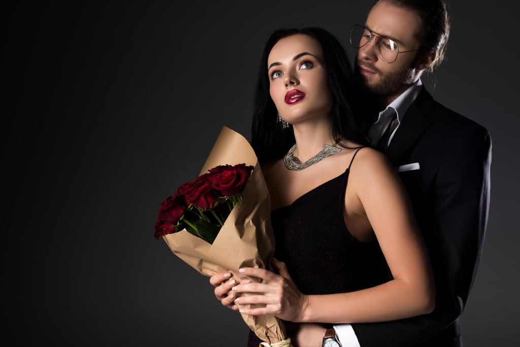 hermosa pareja joven sosteniendo ramo de rosas rojas en el día de San Valentín, aislado en gris
 - Foto, imagen