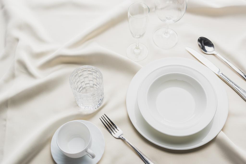 Vista de alto ângulo de louça com copos e xícara de café na toalha de mesa branca
 - Foto, Imagem