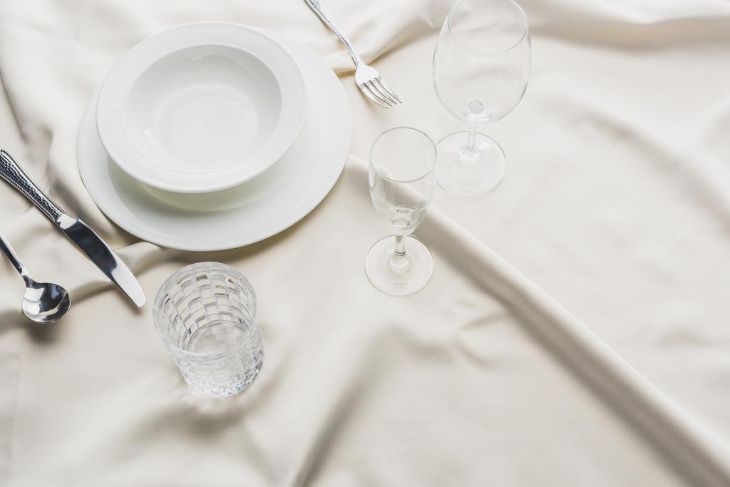 Vista de alto ângulo de servir utensílios de mesa com óculos na toalha de mesa branca
 - Foto, Imagem