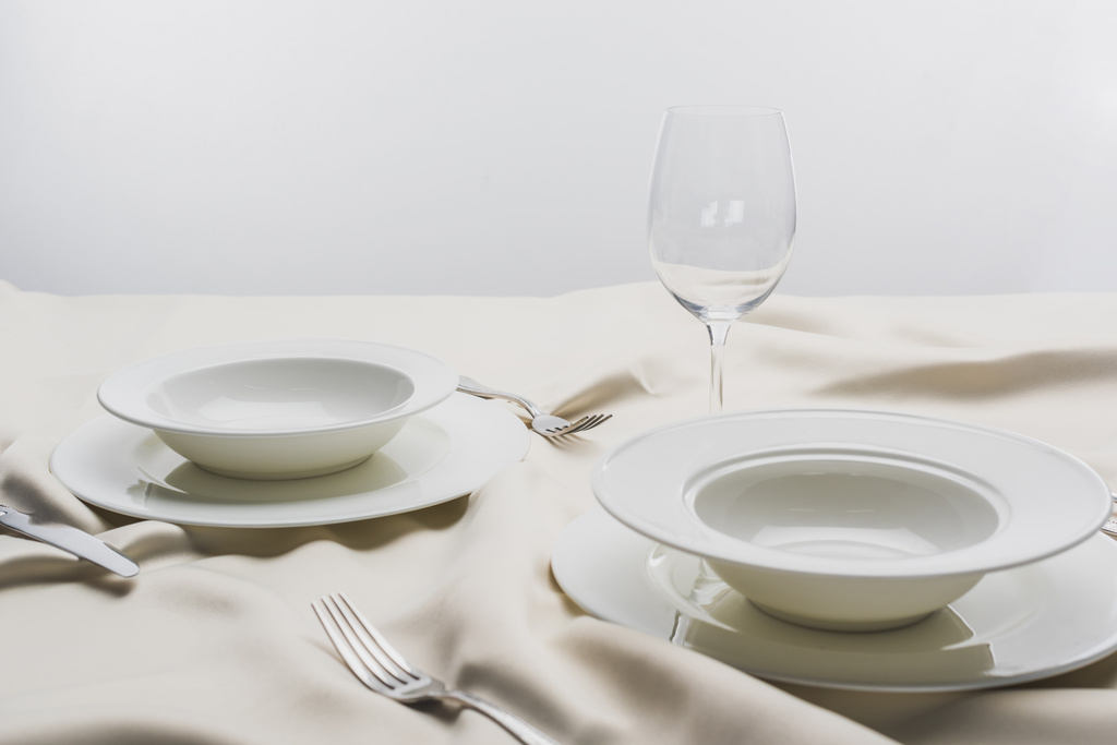 Placas con cubiertos y copa de vino transparente sobre mantel blanco sobre fondo gris
 - Foto, imagen