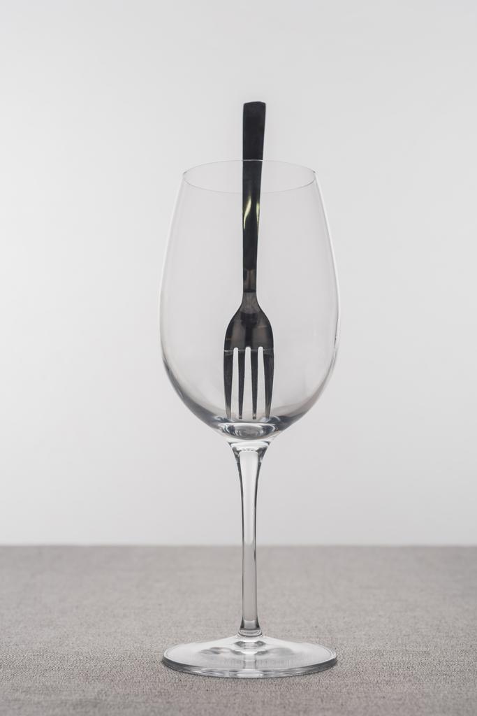 Вилка в прозрачном бокале вина на скатерти изолированы на сером
 - Фото, изображение