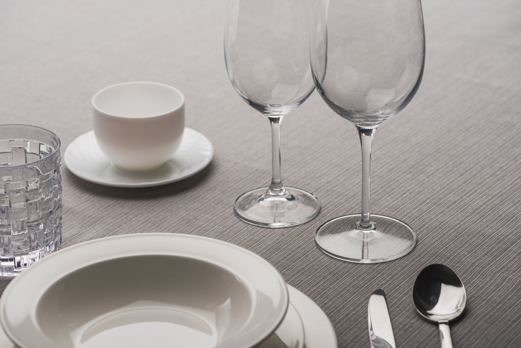 Прозорі келихи для вина поруч з посудом та чашкою кави на сірій тканині
 - Фото, зображення
