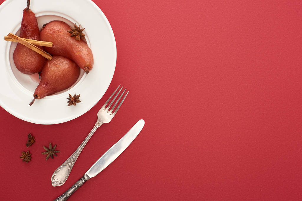 vista dall'alto di deliziosa pera in vino con cannella e anice su piatto su fondo rosso con posate
 - Foto, immagini
