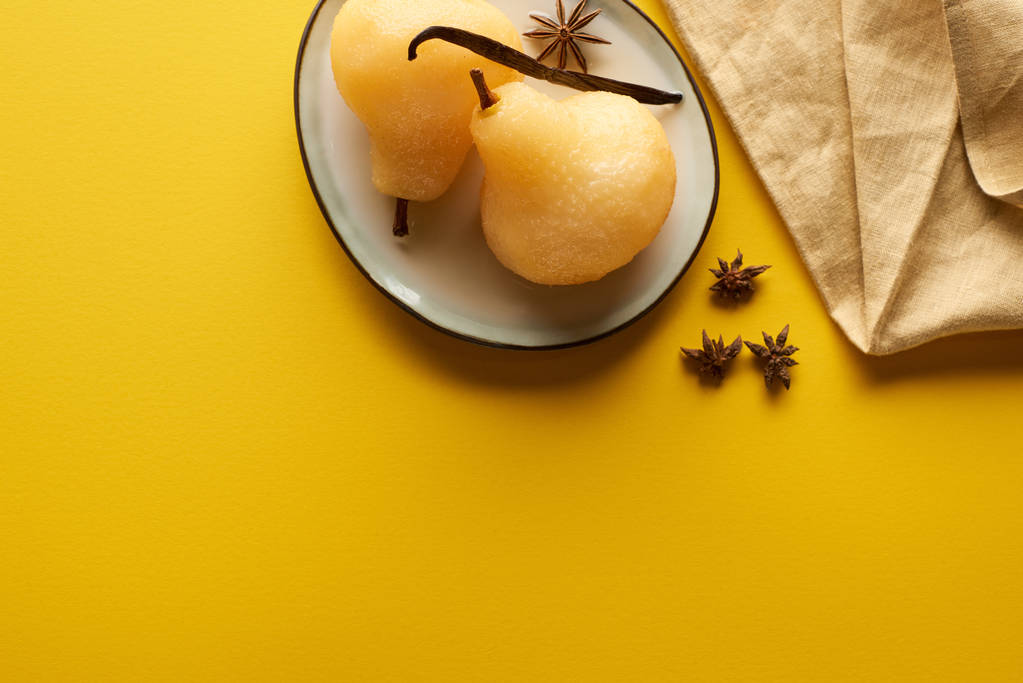 top view νόστιμο αχλάδι σε κρασί με γλυκάνισο στο πιάτο κοντά χαρτοπετσέτα σε κίτρινο φόντο - Φωτογραφία, εικόνα