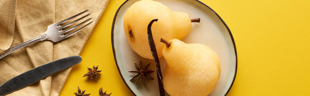 vista superior de la deliciosa pera en vino con anís en el plato cerca de cubiertos y servilleta sobre fondo amarillo, plano panorámico
 - Foto, Imagen