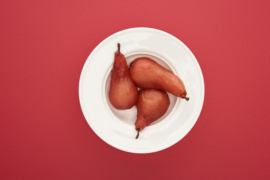 ylhäältä näkymä herkullisia päärynöitä viiniä lautasella punaisella pohjalla
 - Valokuva, kuva