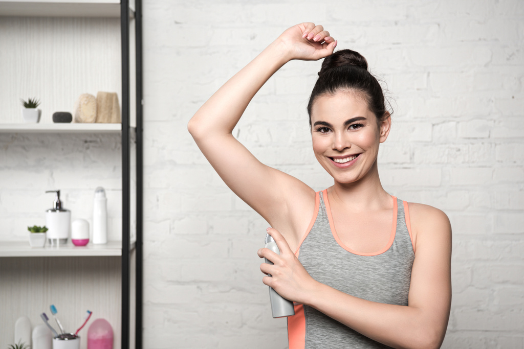 radostná žena s úsměvem na kameru při aplikaci deodorantu na podpaží - Fotografie, Obrázek