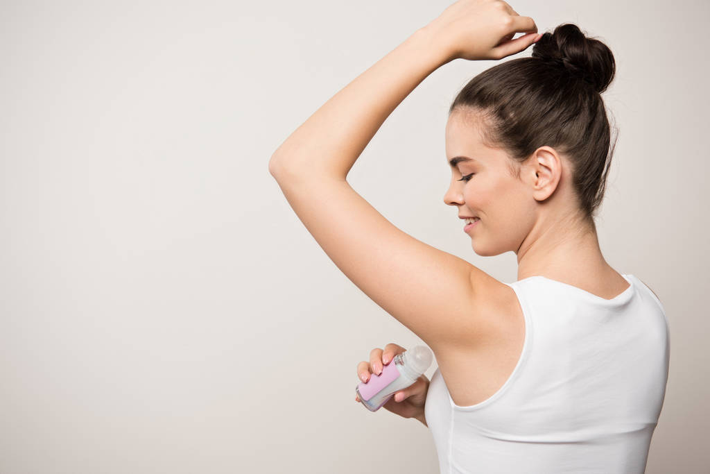 uśmiechnięta kobieta stosująca dezodorant na pachy izolowane na szaro - Zdjęcie, obraz