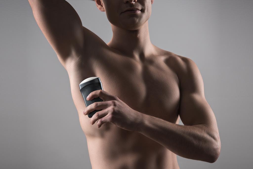 Kolunun altında deodorant tutan üstsüz adamın gri renkte izole edilmiş görüntüsü. - Fotoğraf, Görsel