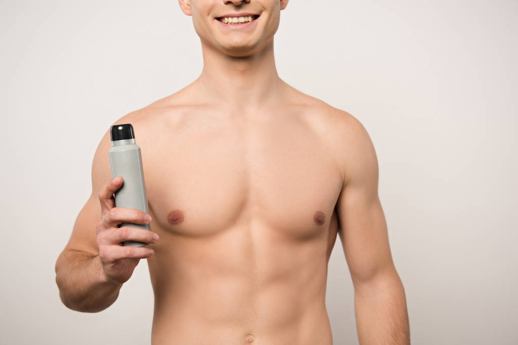 vista ritagliata dell'uomo sorridente senza camicia che tiene isolato il deodorante sul grigio
 - Foto, immagini