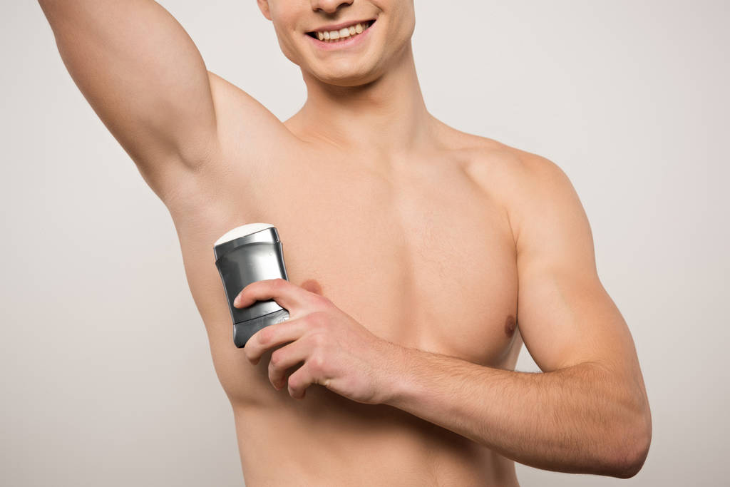 cropped view of shirtless young man holding deodorant near underarm isolated on grey - Photo, Image