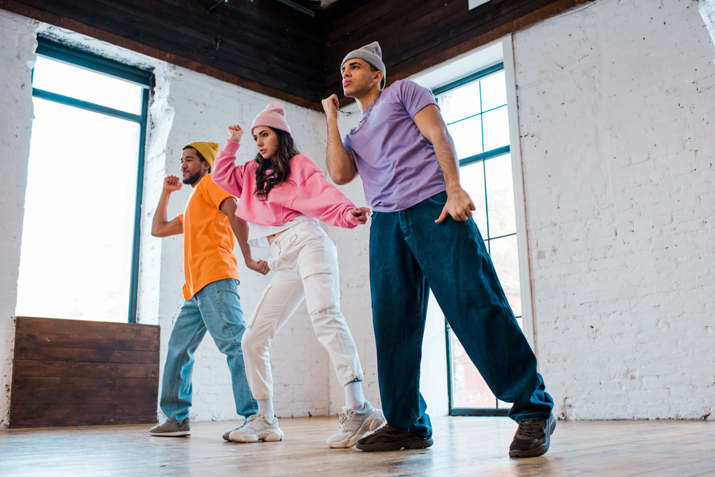gutaussehende multikulturelle Männer in Hüten Breakdance mit schönen Mädchen  - Foto, Bild