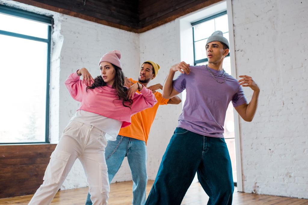Mädchen tanzen Breakdance und gestikulieren mit stylischen multikulturellen Männern in Hüten  - Foto, Bild
