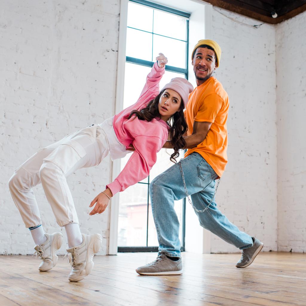 pareja interracial en sombreros breakdancing en estudio de baile
  - Foto, Imagen