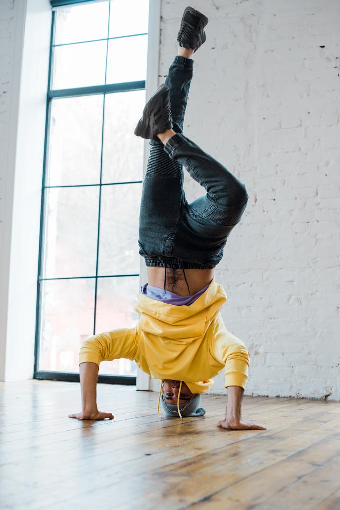 elegante hombre en sombrero haciendo handstand mientras breakdance en estudio de baile
  - Foto, Imagen