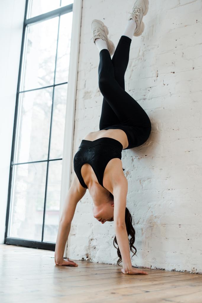 νέα χορεύτρια κάνει handstand κοντά στον τοίχο τούβλο στο στούντιο χορού  - Φωτογραφία, εικόνα