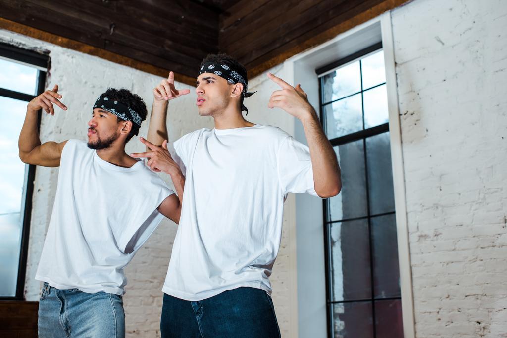spotlight on handsome multicultural dancers in headbands gesturing in dance studio  - Photo, Image