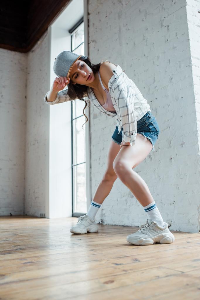 ελκυστική χορεύτρια αγγίζοντας το καπέλο ενώ χορεύει hip-hop  - Φωτογραφία, εικόνα