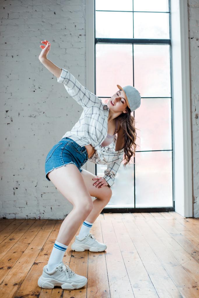 νεαρή γυναίκα με τζιν σορτς και καπέλο που χορεύει χιπ-χοπ  - Φωτογραφία, εικόνα