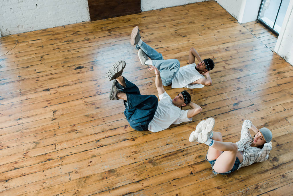 από πάνω άποψη της trendy κορίτσι που βρίσκεται στο πάτωμα με πολυπολιτισμικές χορευτές, ενώ breakdancing σε στούντιο χορού  - Φωτογραφία, εικόνα