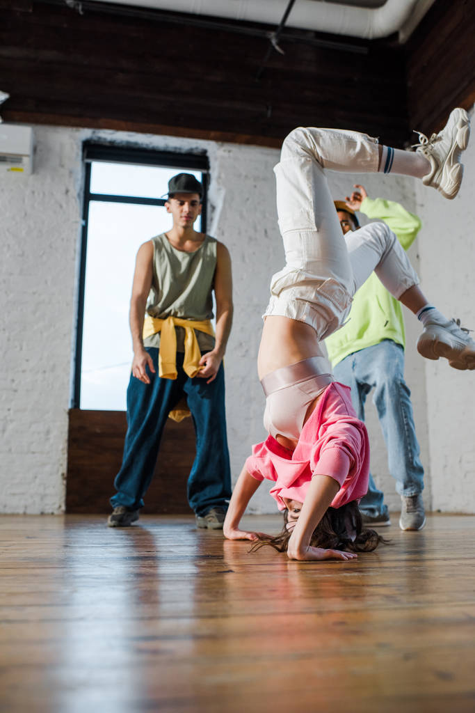 selective focus of girl doing handstand while breakdancing near multicultural men  - Fotoğraf, Görsel