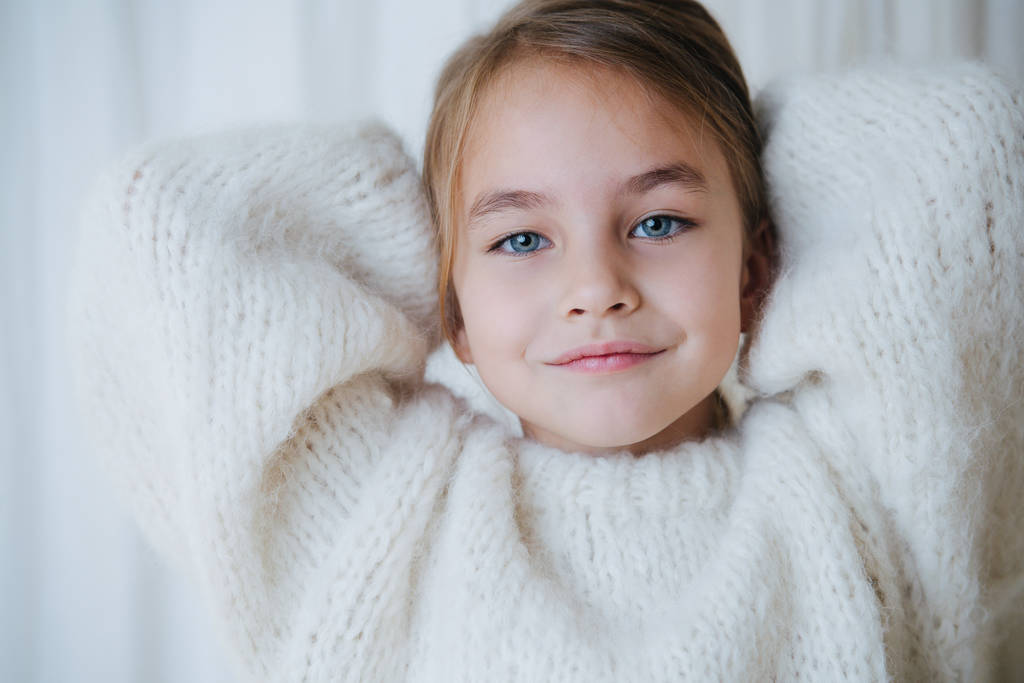 Маленькая девочка в свитере с обеими руками за головой. Закрыть
 - Фото, изображение