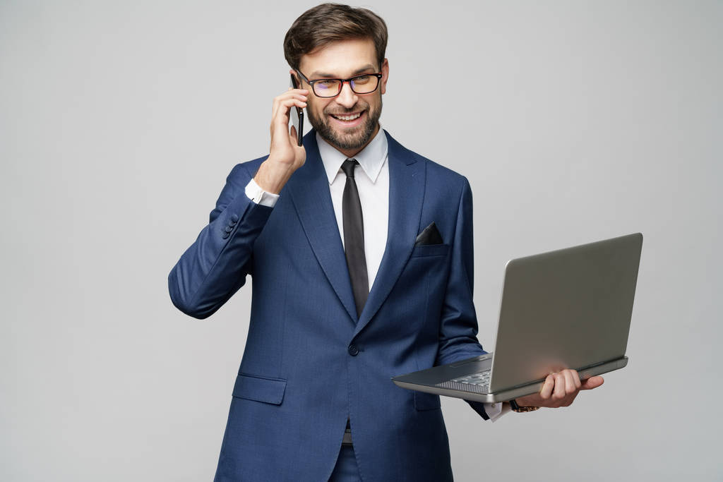 empresário falando no telefone e segurando laptop isolado sobre fundo cinza
 - Foto, Imagem