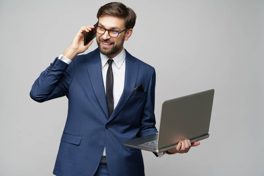 hombre de negocios hablando por teléfono y sosteniendo portátil aislado sobre fondo gris
 - Foto, Imagen