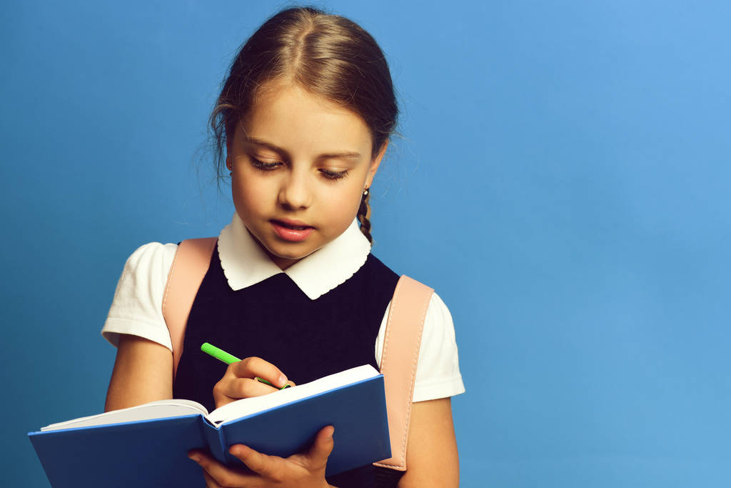 Chica de la escuela con expresión de la cara diligente sobre fondo azul
 - Foto, Imagen