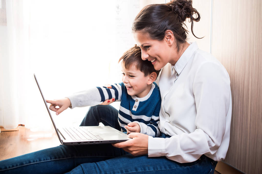 Jovem mãe e seu filho, sentados no chão olhando para o laptop. Chamada de vídeo
 - Foto, Imagem