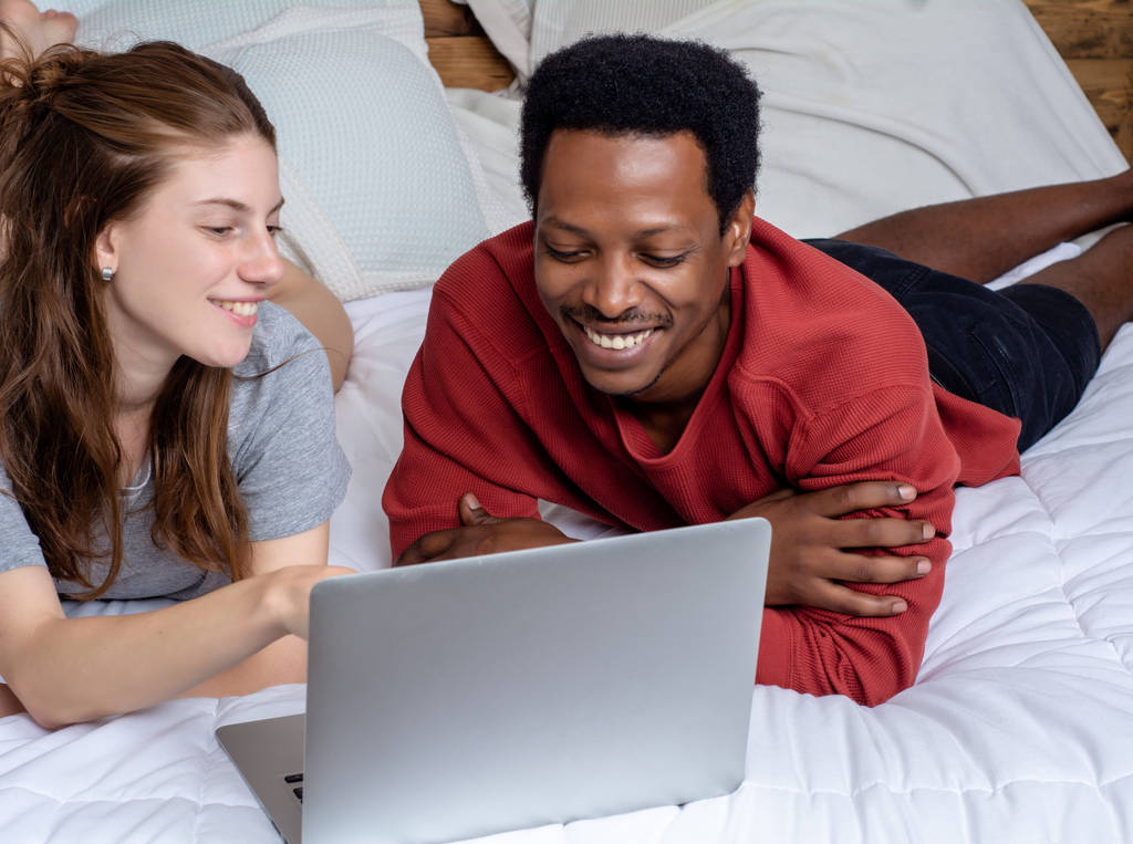 Nuori pari käyttää kannettavaa tietokonetta sängyssä kotona
. - Valokuva, kuva