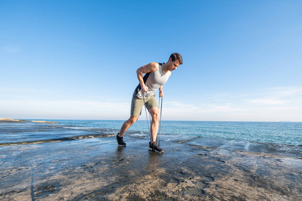 夏の日にビーチで運動用ゴムと若いフィット男性のトレーニング - 写真・画像