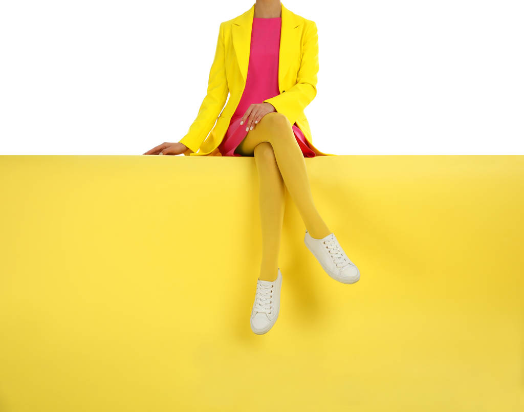 Woman wearing yellow tights and stylish shoes sitting on color b - Photo, Image