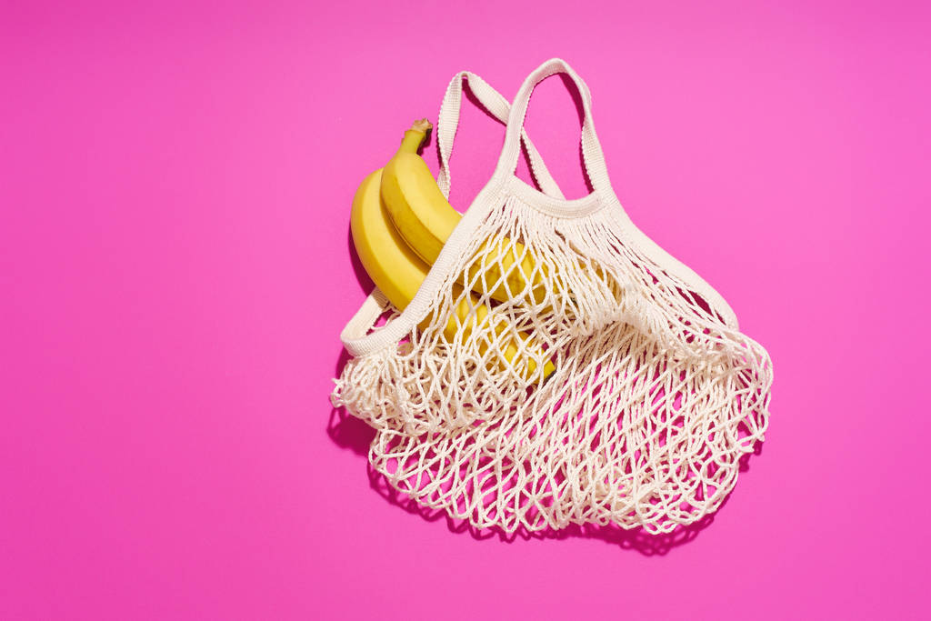 Textile net bag with bananas on bright pink background. Plastic free concept                                 - Fotoğraf, Görsel
