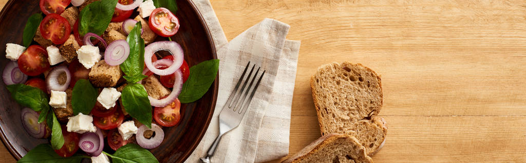 vista dall'alto della deliziosa insalata di verdure italiana panzanella servita sul piatto sul tavolo di legno vicino a pane e forchetta sul tovagliolo, colpo panoramico
 - Foto, immagini
