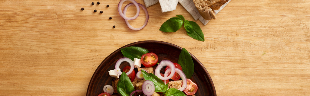 vista superior da deliciosa salada de legumes italiana panzanella servido na placa em mesa de madeira perto de ingredientes frescos, tiro panorâmico
 - Foto, Imagem