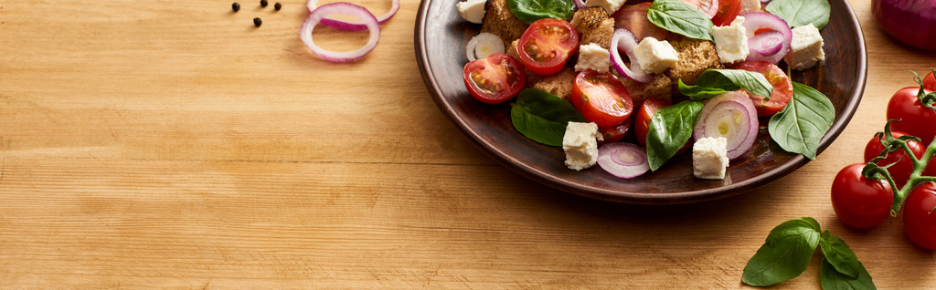 deliciosa salada de legumes italiana panzanella servido em prato na mesa de madeira perto de ingredientes frescos, tiro panorâmico
 - Foto, Imagem