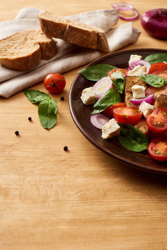 köstliche italienische Gemüsesalat Panzanella serviert auf Teller auf Holztisch in der Nähe von frischen Zutaten und Brot - Foto, Bild